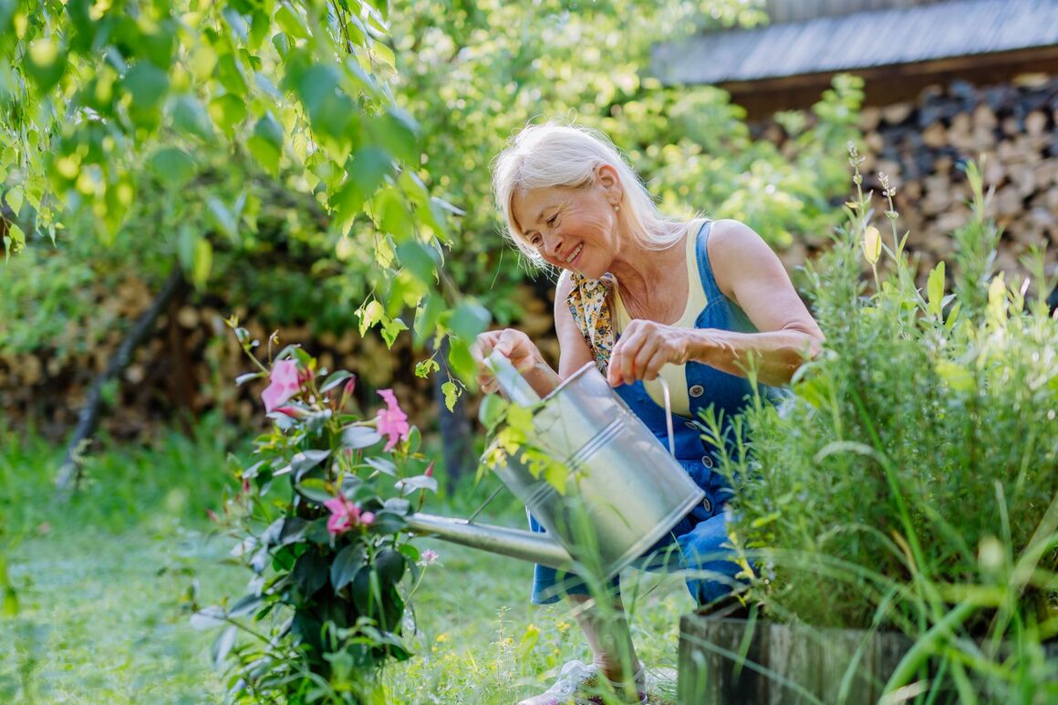 Ältere Frau gießt blühende Pflanzen im Garten – aktiv und naturverbunden im Alter