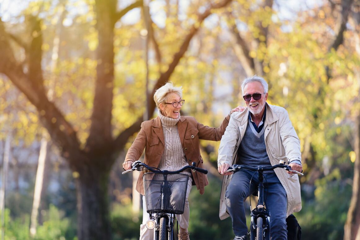 Älteres Paar fährt lachend Fahrrad im Park – aktiv und gesund im Alter bei herbstlichem Wetter