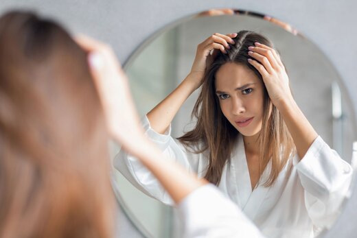 Eine Frau betrachtet ihre Haare im Spiegel